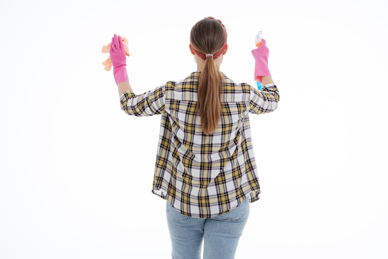 Back view of a woman in latex gloves cleaning with spray and cloth, indoor studio shot.
